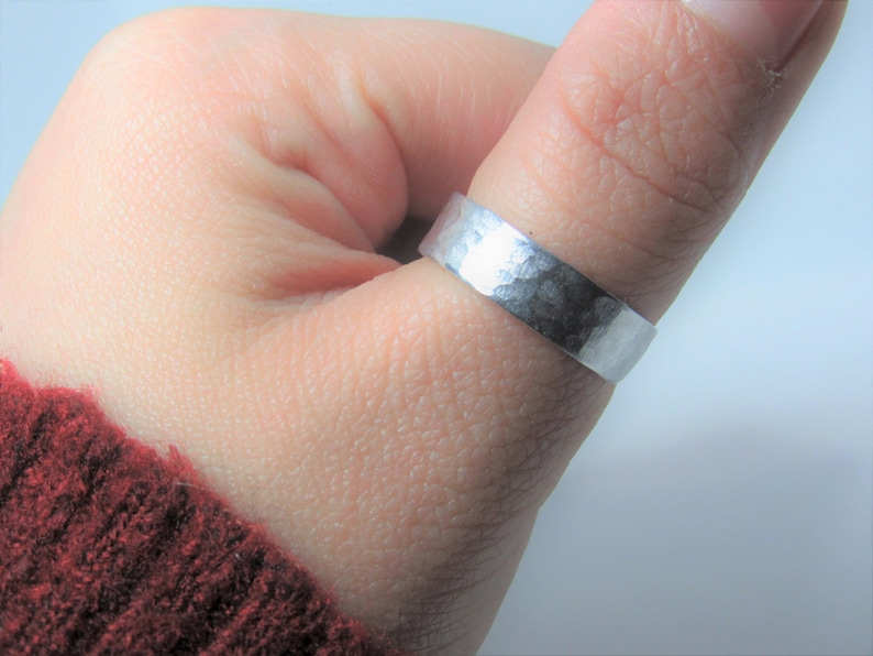 May include: A silver hammered ring worn on a finger.