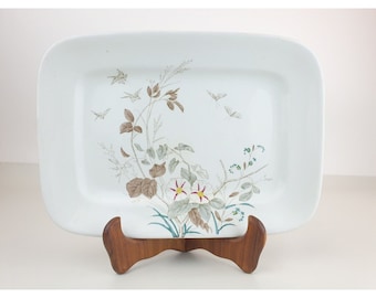 Puede incluir: Plato rectangular blanco para servir con un diseño floral que presenta flores blancas con centros rojos, hojas verdes y ramas marrones. También hay pequeñas mariposas blancas en el plato.
