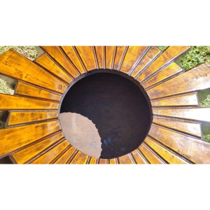 Puede incluir: Un macetero de madera con un dise&ntilde;o de sol. El macetero est&aacute; hecho de madera y tiene un acabado marr&oacute;n oscuro. El macetero tiene una gran abertura redonda en el centro.