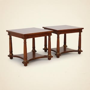 May include: Two matching wooden side tables with square tops and lower shelves. The tables are a warm brown color with decorative gold accents on the legs. Each table has four legs and a lower shelf for storage.