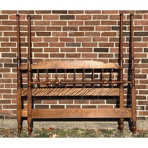 May include: A wooden bed frame with a headboard and footboard. The headboard has a curved top and a series of vertical spindles. The footboard is plain and rectangular. The frame is made of dark wood and has a natural finish.