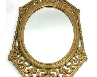 May include: A gold-toned oval mirror with an ornate, intricately carved frame. The frame has a rope-like design on the sides and floral motifs throughout.