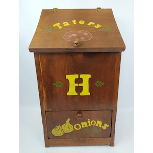 May include: A wooden storage box with a hinged lid and a drawer. The box is painted brown with yellow lettering that says "Taters" and "Onions". The drawer has a green and yellow painted onion design.