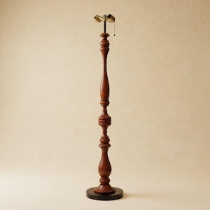 May include: A tall, wooden floor lamp with a dark brown finish. The lamp features a turned wood design with decorative details and a round base. The lamp has a brass-colored light fixture at the top and a pull chain.