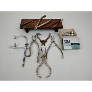 May include: A set of dental tools including pliers, forceps, and a small tray with a wooden base. The tools are made of metal and have a silver finish. The tray is made of wood and has a dark brown finish. A box of Kerr Impression Compound is also included in the image.