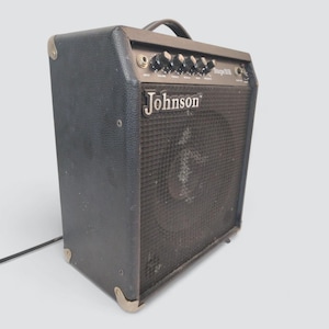 May include: Black Johnson Stage 308 amplifier with a handle, control knobs, and a speaker grill. The amplifier has metal corner protectors and the Johnson logo. A power cord extends from the side.