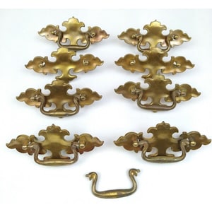 May include: Set of eight antique brass cabinet pulls with ornate designs. The pulls have a loop handle and are in excellent condition.