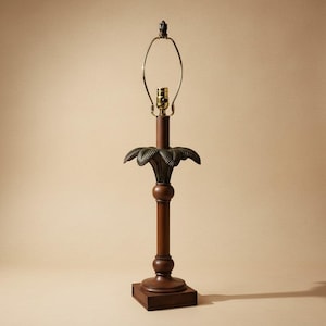 May include: A dark brown table lamp with a palm leaf design. The lamp has a square base, a long, cylindrical stem, and a decorative palm leaf accent. The lamp's metal hardware is gold-toned, and the lamp is approximately 28 inches tall.