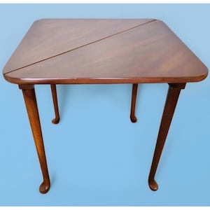 May include: A brown wooden folding table with four cabriole legs. The table top is made of two sections that fold together.