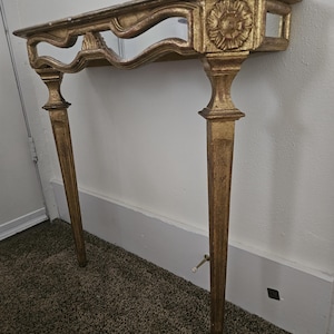 May include: A gold-painted console table with a mirrored shelf and ornate floral carvings. The table has four slender legs and a scalloped edge design. The table is approximately 48 inches long.