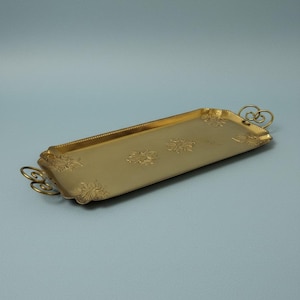 May include: A rectangular gold-colored serving tray with floral embossed designs and decorative handles. The tray has a slightly raised edge with a beaded border. The handles are a looped design. The tray is empty.