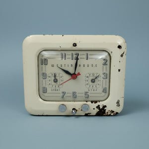 May include: A rectangular off-white Westin House clock with a distressed metal frame showing paint loss and rust. The face features black numerals, two smaller sub-dials labeled START and STOP, and black hour and minute hands with a red second hand.