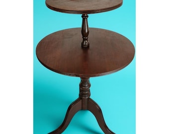 May include: A two-tiered, dark brown wooden side table with a round top and a pedestal base. The top tier is smaller than the bottom tier. The table has a classic, antique design, and stands approximately 30 inches tall.