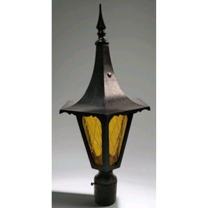 May include: A black outdoor lamp post with a pointed top and a yellow glass paneled light fixture. The lamp has a decorative design and is mounted on a black base.