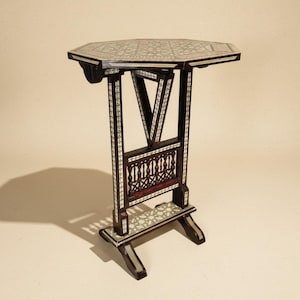 May include: An octagonal side table crafted from dark wood, featuring intricate white mother-of-pearl inlay patterns on the top, legs, and base. The structure includes a central spindle-style support and a V-shaped brace connecting the legs.