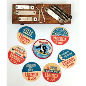 May include: Ten round, colorful, paper, Hamm's Beer coasters with various slogans. The coasters feature a red, white, and blue color scheme with a variety of designs, including a bear surfing, a moon, and a bar.