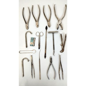May include: A collection of vintage dental tools, including pliers, forceps, a small pair of scissors, a metal rod, a hammer, and a small metal box with a label that reads "3/2 1/2 1/2".