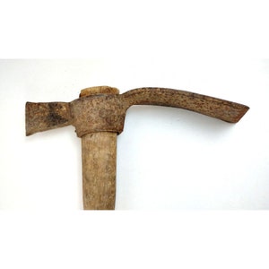 May include: A rusty metal pickaxe with a wooden handle. The pickaxe has a curved blade and a pointed end.