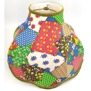 May include: A patchwork lampshade with a variety of floral patterns in shades of red, blue, green, and yellow. The lampshade has a scalloped edge and a gold trim.