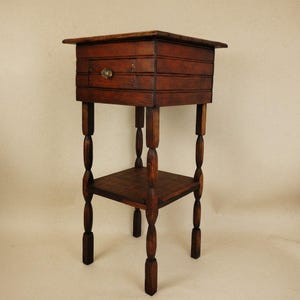 May include: A dark brown wooden side table featuring a square top, a single drawer with a small round knob, and a lower shelf. The table is supported by four turned legs with a spindle design, showcasing a deep wood grain finish throughout.