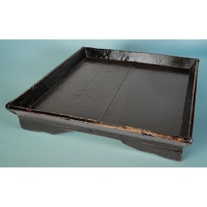 May include: A black wooden tray with a raised edge and a slightly curved base. The tray is made of wood planks and has a smooth, lacquered finish.