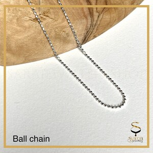 May include: A silver ball chain necklace on a wooden surface.  The chain is made of small, round beads.
