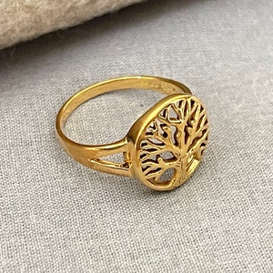 May include: A gold-toned ring featuring a tree of life design. The ring is crafted from metal and has a delicate, intricate design.