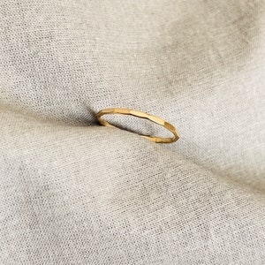 May include: A simple gold band ring with a hammered finish.