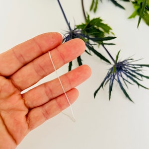 May include: A silver chain necklace, shown on a hand, is a delicate and simple piece of jewellery.