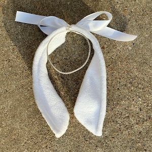 May include: White bunny ear headband with a white satin bow and a silver metal hoop.