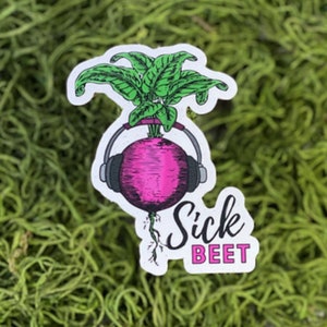 May include: A pink beetroot with green leaves wearing headphones and the text "Sick Beet" in black and pink lettering.