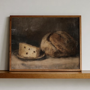 Op de afbeelding: Een rechthoekig ingelijst olieverfschilderij met een stilleven van een rond brood met een bruine korst en een stuk lichtgele kaas met donkere vlekken op een klein bordje, uitgevoerd in aardetinten tegen een donkere achtergrond.
