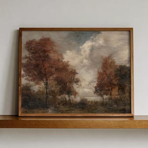 May include: A rectangular landscape painting in a thin wooden frame depicting a forest scene with autumn-colored trees in shades of rust and brown under a cloudy, overcast sky. The artwork features a muted color palette and visible brushstrokes.