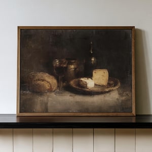 Op de afbeelding: Een ingelijst olieverfschilderij met een donker stilleven van een brood, een glas rode wijn, een metalen container en twee stukjes kaas op een bord. De compositie maakt gebruik van diepe bruine en gedempte tinten voor een sombere sfeer.