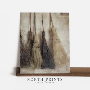 May include: A wall art print featuring four rustic brooms leaning against a textured, neutral-toned wall. The brooms vary in color from light tan to dark brown and black, with a bundle of dried twigs on the left. The text NORTH PRINTS art collective appears below.