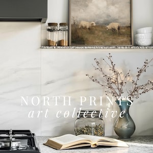 K&ouml;nnte beinhalten: K&uuml;chenszene mit gerahmtem Gem&auml;lde von Schafen, Gew&uuml;rzgl&auml;sern, einer Vase mit Zweigen und einem offenen Buch. Der Text "NORTH PRINTS art collective" ist sichtbar. Modernes Design.