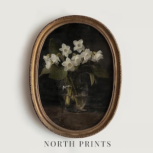 May include: A vintage oval-shaped gold frame with a dark background featuring a bouquet of white flowers in a clear glass vase.