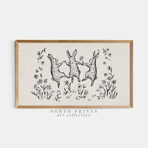 May include: A framed print featuring a black and white illustration of three rabbits dancing in a circle, holding hands. The rabbits are surrounded by flowers and foliage. The print has a vintage aesthetic.