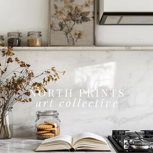 Op de afbeelding: Een keuken met een ingelijste bloemenprint, potten met kruiden en een glazen pot met koekjes. Een open boek en een gasfornuis zijn ook zichtbaar. De tekst "NORTH PRINTS art collective" wordt weergegeven.