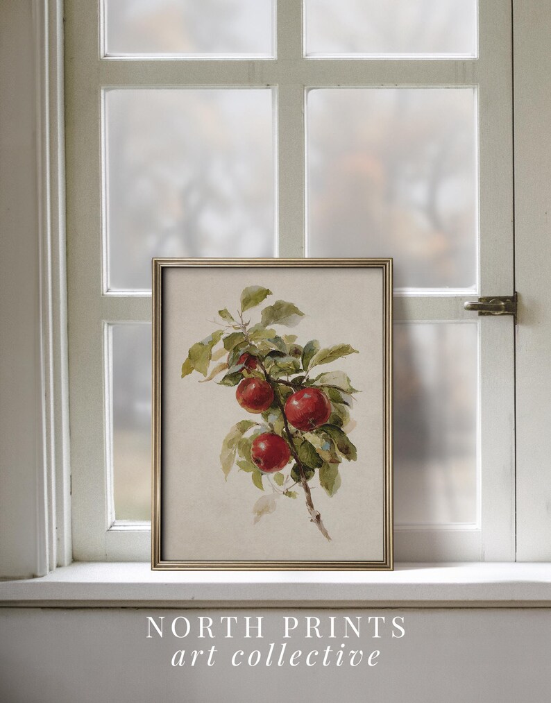 Peut inclure: Une impression d'art encadr&eacute;e repr&eacute;sentant une aquarelle de pommes rouges sur une branche avec des feuilles vertes. L'impression est dans un cadre dor&eacute; et repose sur un rebord de fen&ecirc;tre blanc. Le texte "NORTH PRINTS art collective" est en bas.