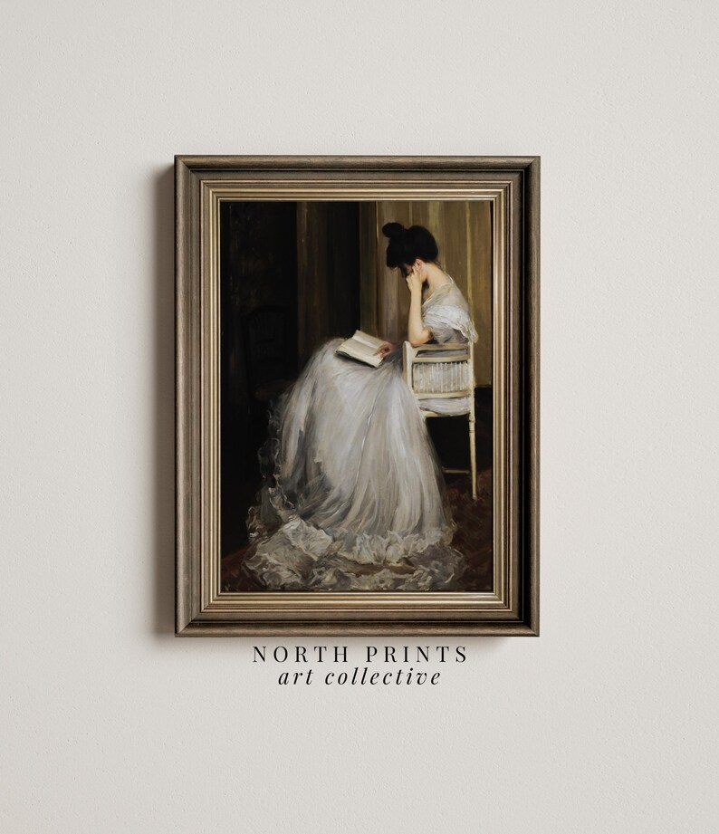 May include: A framed painting of a woman in a white dress sitting in a chair and reading a book. The painting is set in a room with a dark background and a light-colored wall.