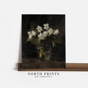 May include: A bouquet of white flowers in a clear glass vase on a dark brown wooden surface. The flowers are arranged in a simple, elegant style, and the vase is partially obscured by the flowers.