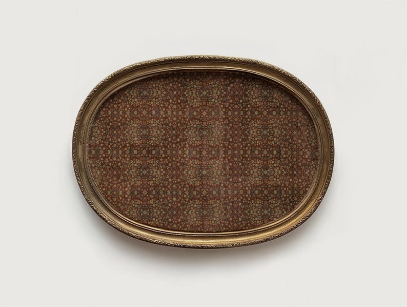 May include: An oval serving tray with a decorative gold-coloured frame. The tray's interior features a detailed pattern in shades of brown, red, and beige. The frame has an ornate, textured design. The tray is set against a plain white background.