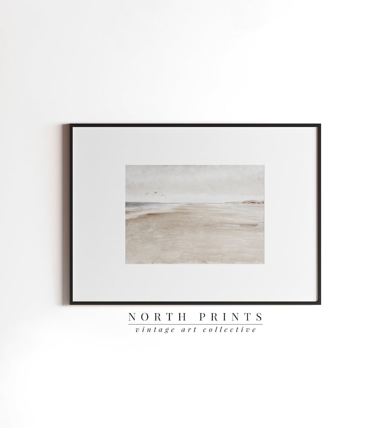 May include: A framed print of a watercolour painting depicting a beach scene with a sandy shore, a calm ocean, and a few birds flying in the sky. The print is framed in a black frame and has the text "NORTH PRINTS vintage art collective" at the bottom.