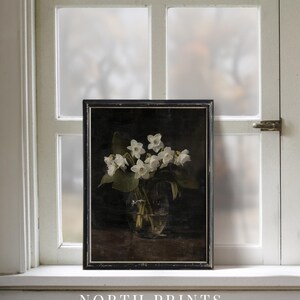 May include: A black framed print of a still life featuring a bouquet of white flowers in a clear glass vase on a dark background. The print is titled "NORTH PRINTS art collective".