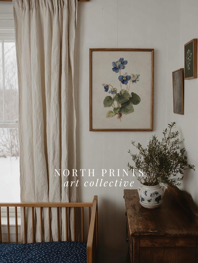 K&ouml;nnte beinhalten: Ein gerahmter botanischer Druck mit blauen Blumen und gr&uuml;nen Bl&auml;ttern h&auml;ngt an einer wei&szlig;en Wand. Der Druck befindet sich in einem Holzrahmen. Das Bild zeigt auch ein Holzbett, einen beigen Vorhang und eine kleine Topfpflanze auf einer Holzkommode. Der Text "NORTH PRINTS art collective" ist sichtbar.