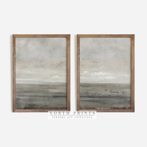 Può includere: Due dipinti astratti di paesaggi incorniciati con una tavolozza di colori tenui di grigio, bianco e marrone. I dipinti sono in cornici di legno e sono appesi a una parete bianca. Il testo "NORTH PRINTS vintage art collective" è stampato sotto i dipinti.