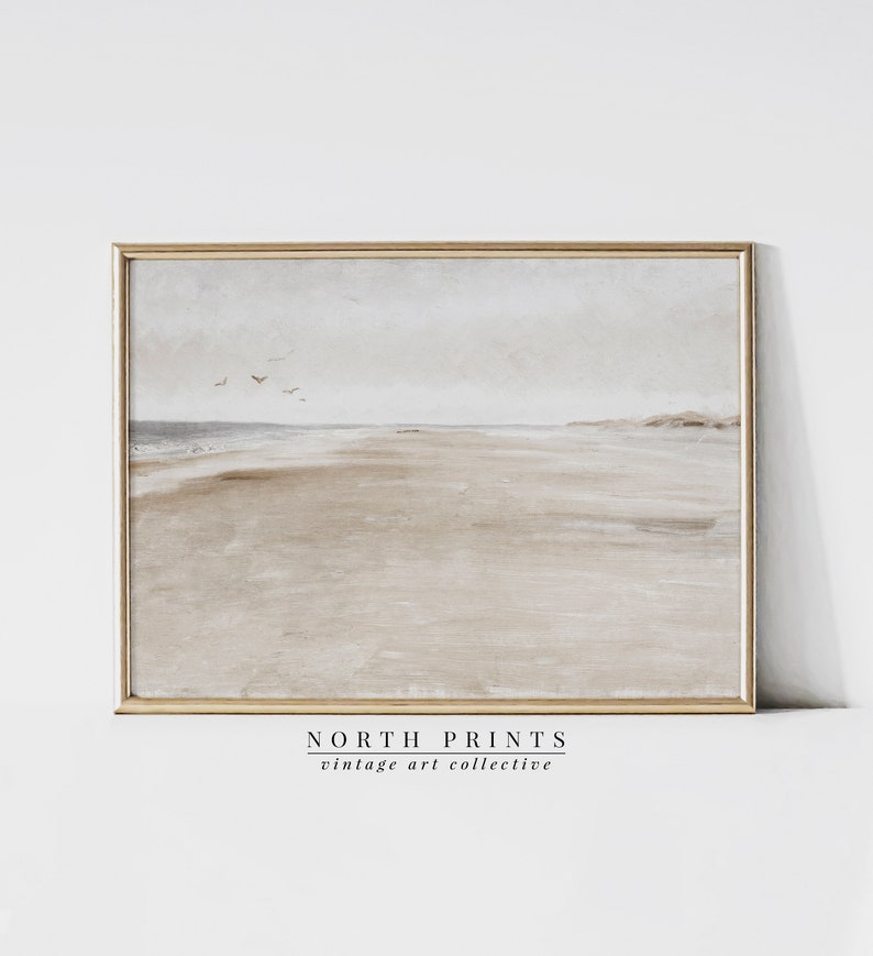 May include: A framed painting depicting a beach scene with a light blue sky, a sandy beach, and a few birds flying in the distance. The frame is a light wood colour. The painting is titled "NORTH PRINTS vintage art collective".