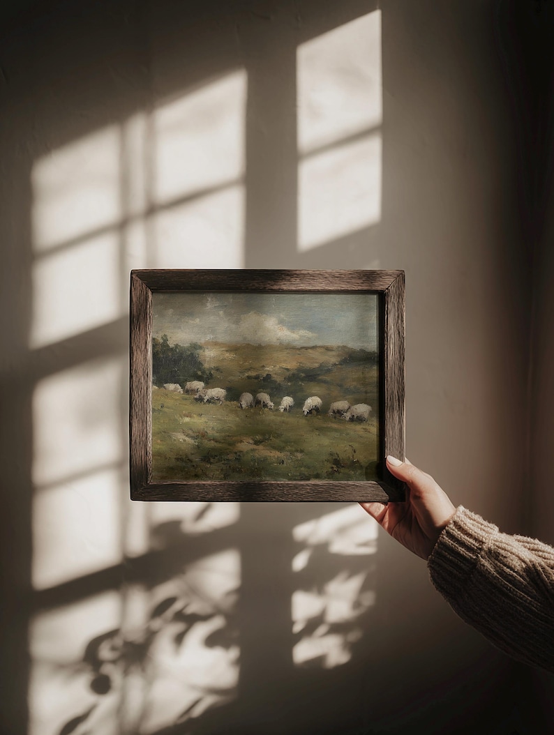 K&ouml;nnte beinhalten: Gerahmtes Landschaftsgem&auml;lde mit Schafen, die auf einer gr&uuml;nen Wiese unter einem bew&ouml;lkten Himmel grasen. Das Kunstwerk wird in einem dunklen Holzrahmen pr&auml;sentiert und erinnert an eine Vintage-&Auml;sthetik.