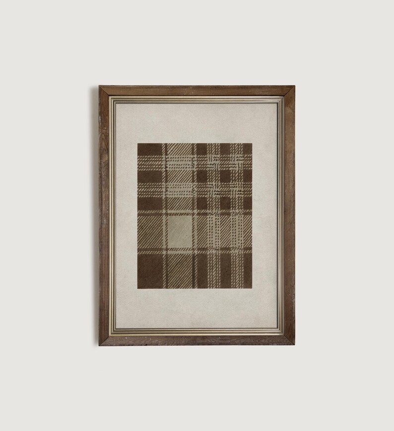 May include: Framed print featuring a brown and tan plaid pattern. The artwork is displayed within a wooden frame, adding a touch of rustic elegance. The plaid design is a classic pattern, suitable for various interior design styles.